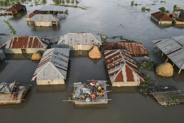 A family take shelter on the roof of their small house. Due to climate change, incessant rainfall has flooded nearby houses. Photo: Muhammad Amdad Hossain / Climate Visuals